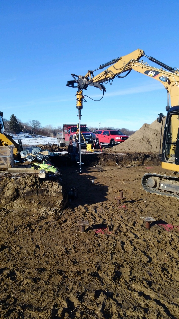 Excavator installing helical piles for a new building foundation